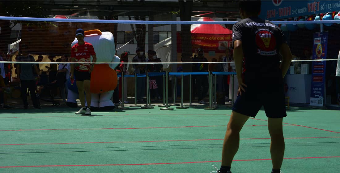屋外イベントでバドミントンをプレイする選手たちと背景の観客やブース